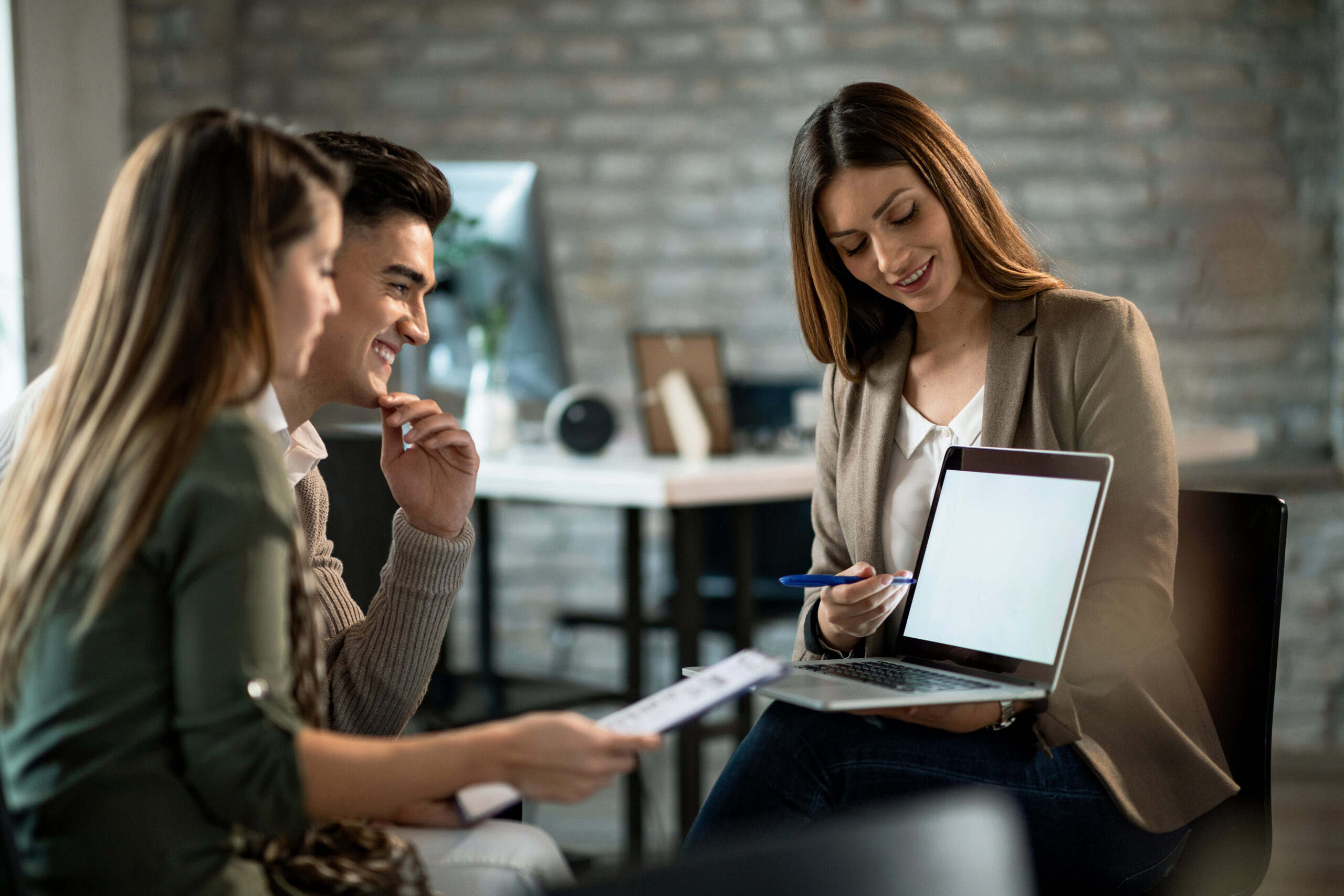 Smiling real estate agent using a computer while having a meeting with young couple and making investment plans.